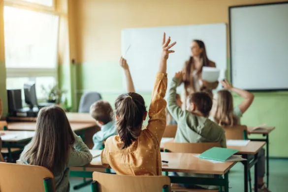 Des élèves lèvent la main face à leur enseignante, dans une salle de classe.