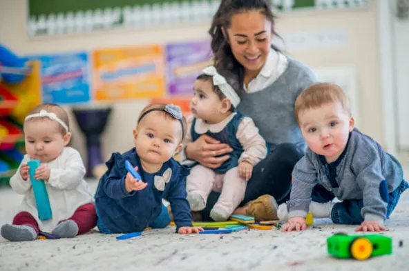 Une professionnelle de la petite enfance assise au sol avec quatre bébés.